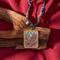 Tibetan deity pendant necklace with colorful artwork and braided cord on wood and red fabric