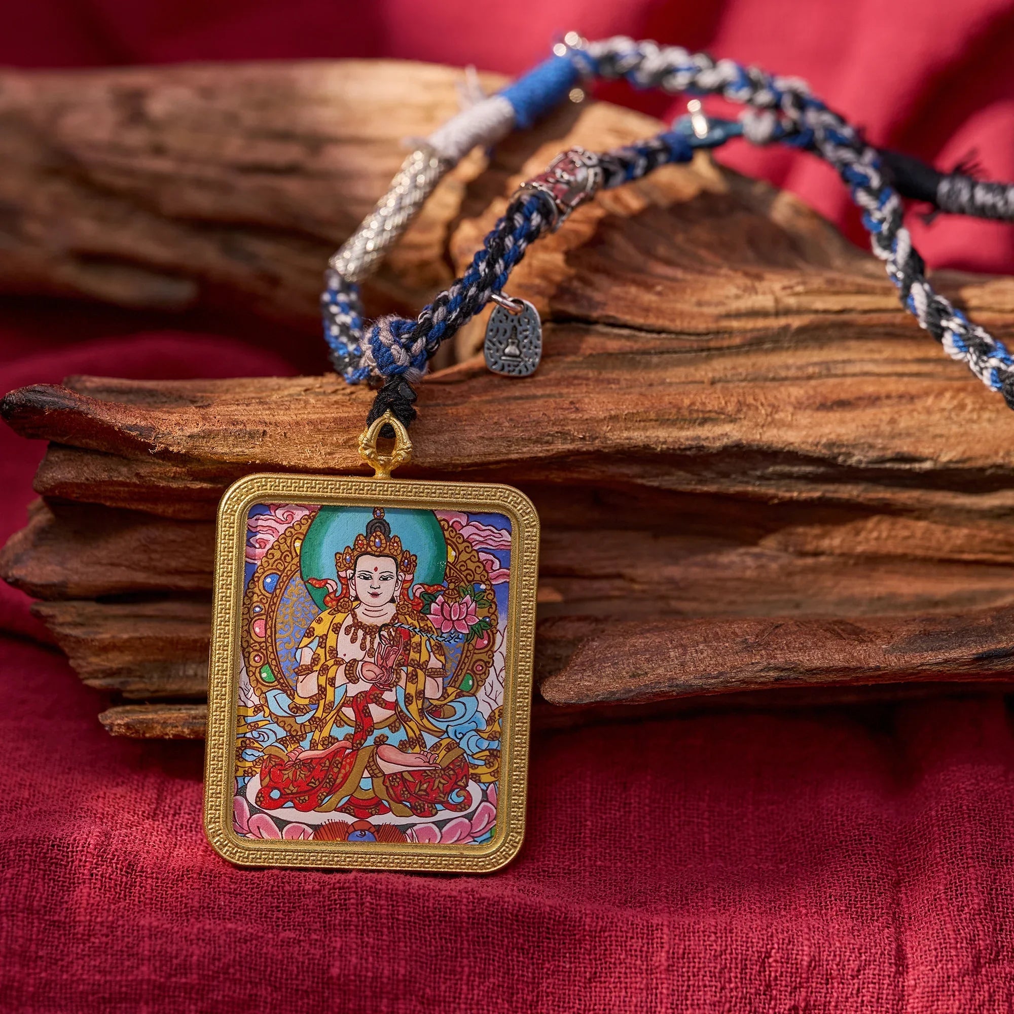 Handcrafted Tibetan deity pendant necklace with braided cord, spiritual jewelry on wood and red fabric background.