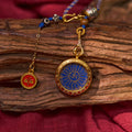 Gold and blue Himalayan pendant with sacred motif and red Buddhist amulet on rustic wood