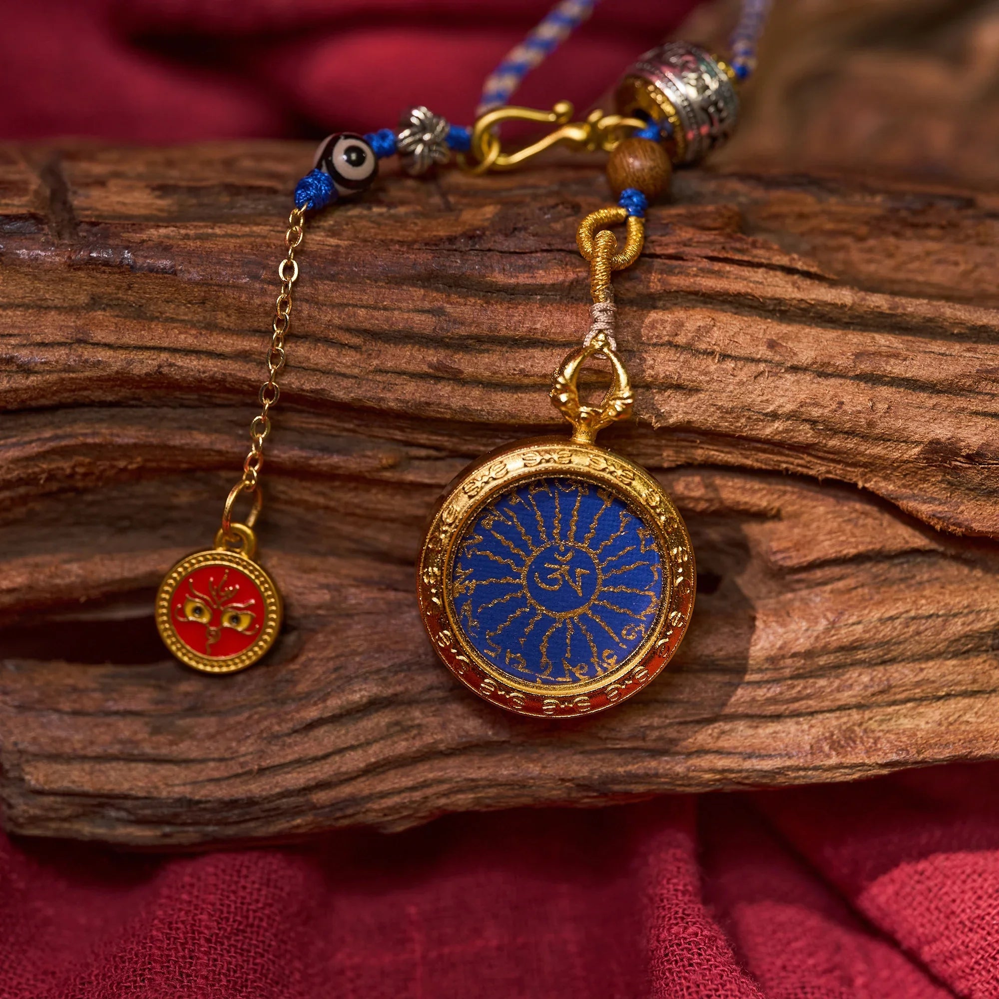 Gold and blue Himalayan pendant with sacred motif and red Buddhist amulet on rustic wood