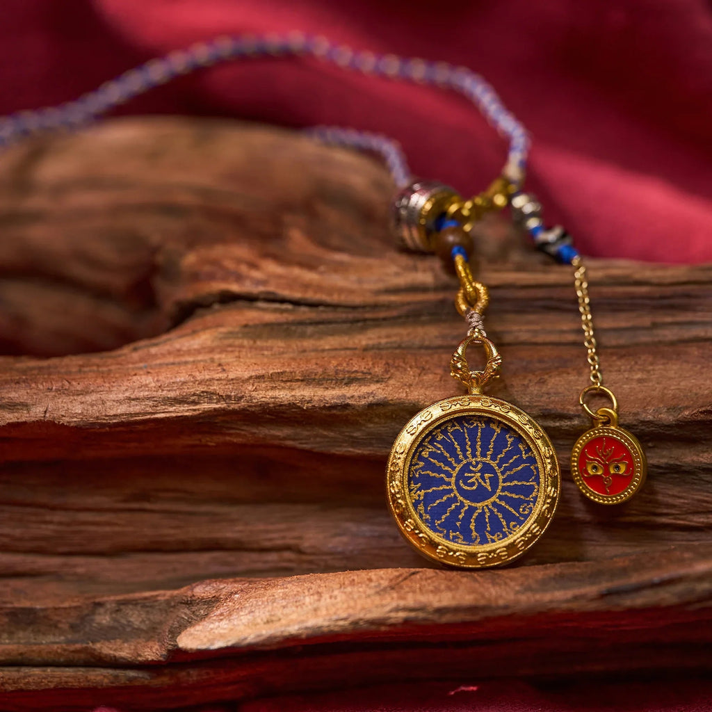 Gold Himalayan amulet necklace with blue and red enamel, spiritual symbols on wood background