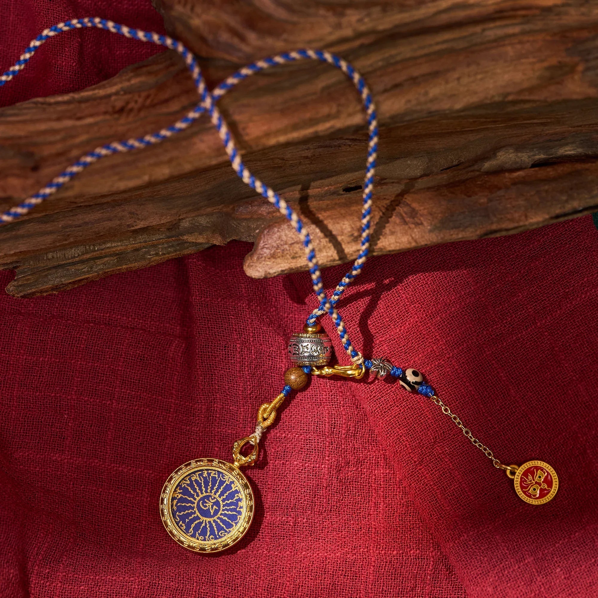 Tibetan style pendant necklace with gold and blue medallion, intricate charms on red fabric