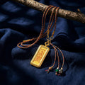 Gold Tibetan amulet pendant with braided cord and beaded tassels on dark blue fabric