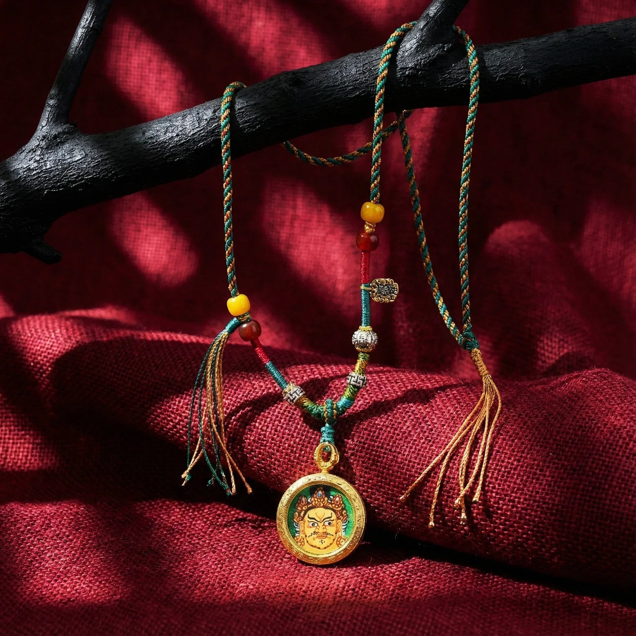 Tibetan-inspired braided necklace with colorful beads and a gold deity pendant on red fabric