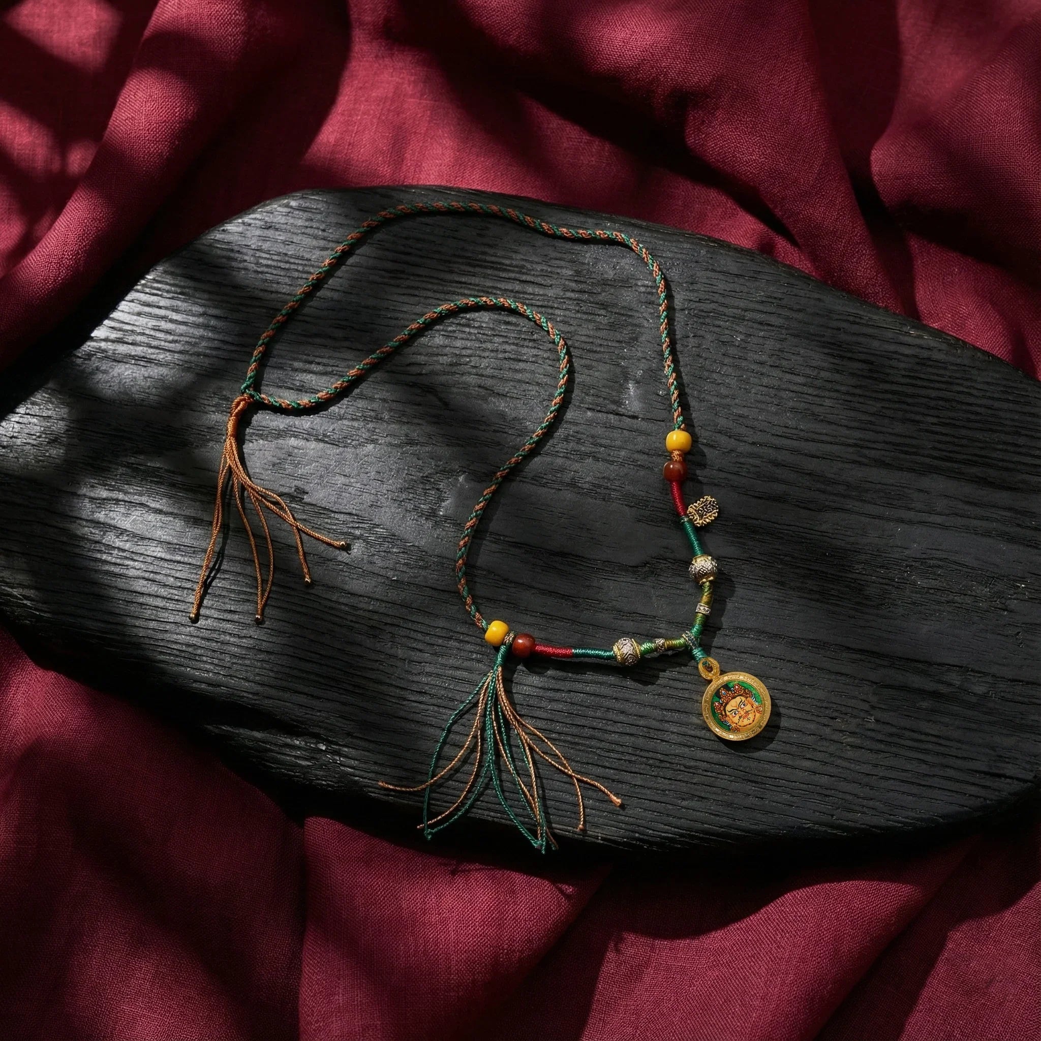 Tibetan style braided necklace with colorful beads and a gold circular pendant on dark wood