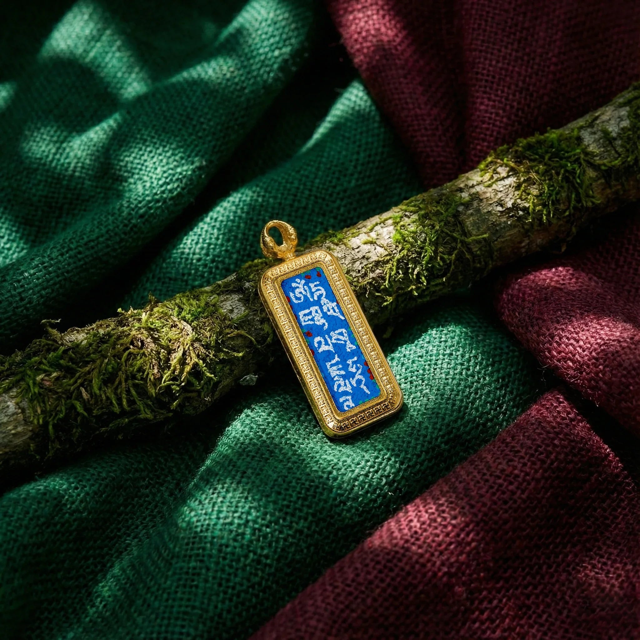 Tibetan mantra rectangular pendant with gold border on mossy branch and colored fabric background