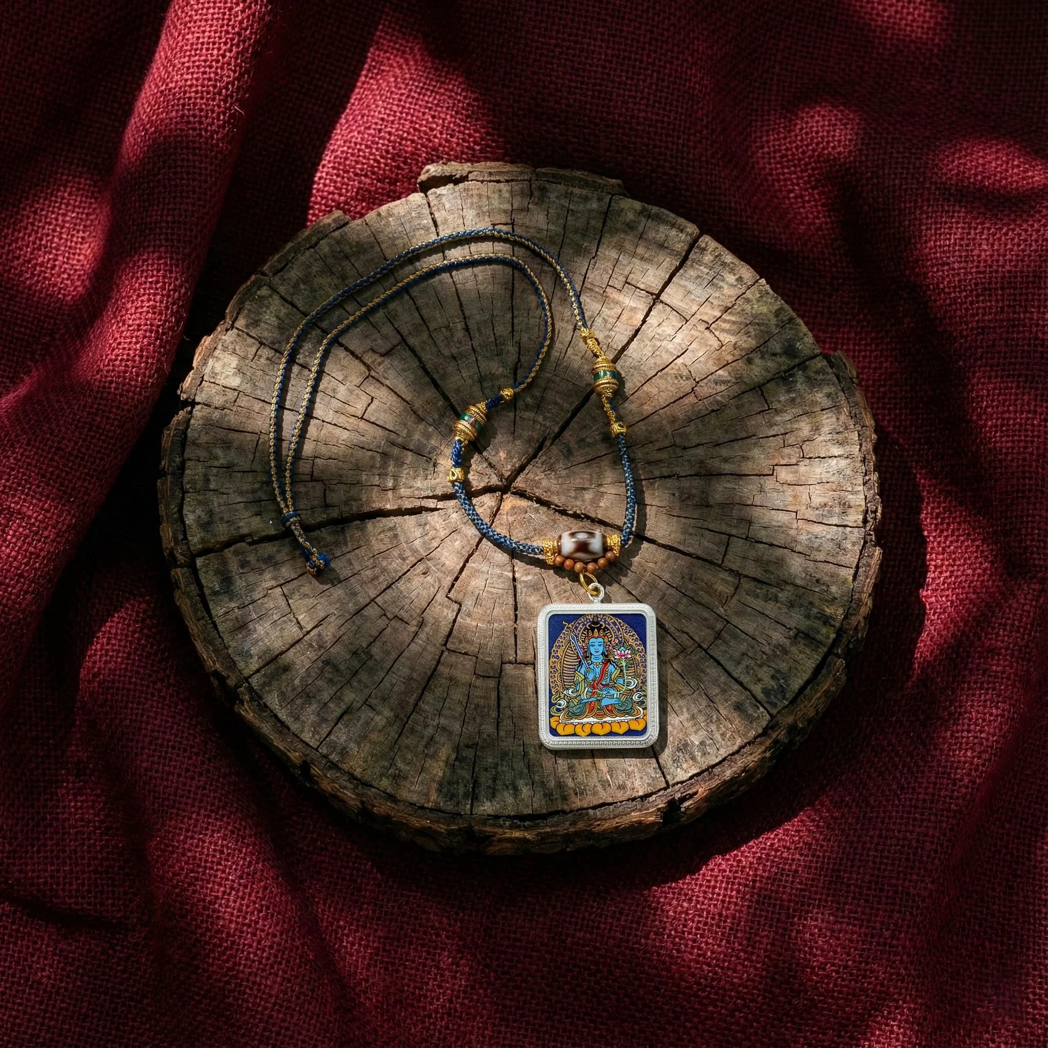 Tibetan Buddhist pendant necklace with colorful deity artwork on braided cord, placed on rustic wood