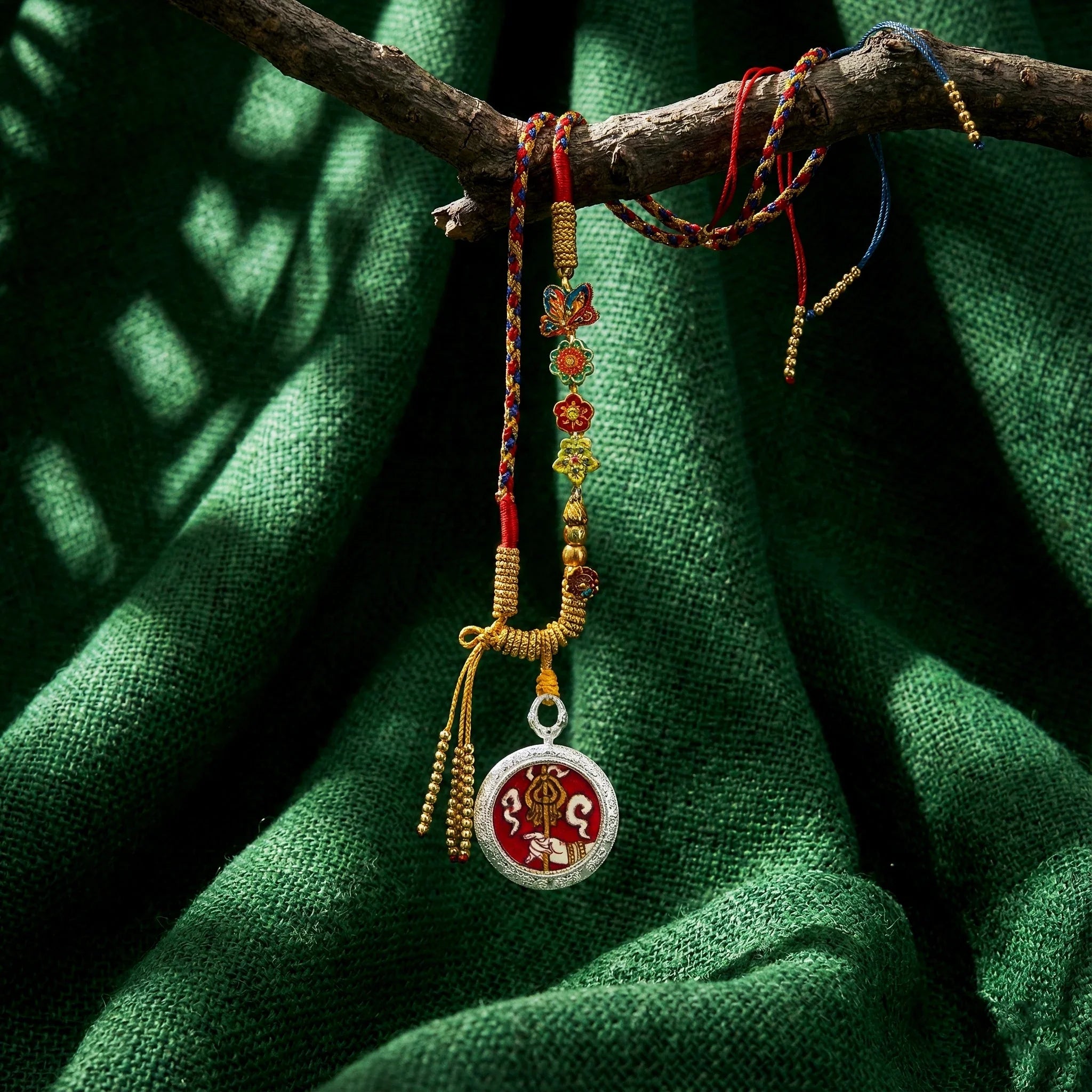 Handwoven Tibetan amulet necklace with colorful braided cord, floral beads, and Buddhist pendant on green fabric background