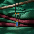 Tibetan mantra pendant necklace with black cord and amber beads on colorful woven fabric