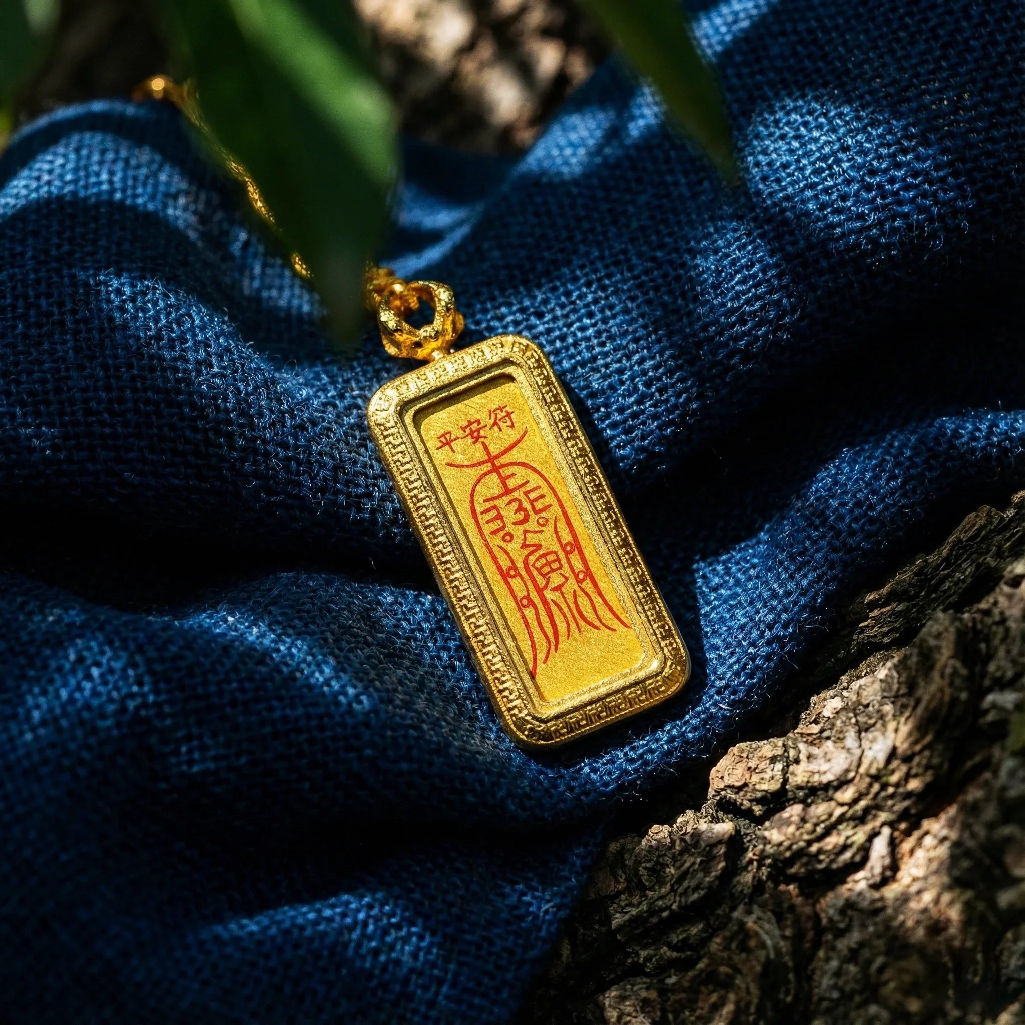 Gold amulet pendant with red Chinese talisman engraving, resting on blue fabric outdoors